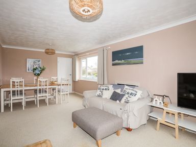 A living room with a sofa and ottoman a dining table with chairs and a television on a stand at Ty Bedw in Benllech