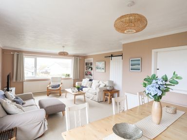 A living room with sofas a coffee table and a dining table with flowers at Ty Bedw in Benllech