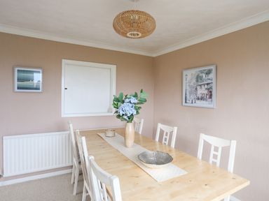 A dining room with a wooden table six chairs a vase with flowers and framed pictures on the walls at Ty Bedw in Benllech