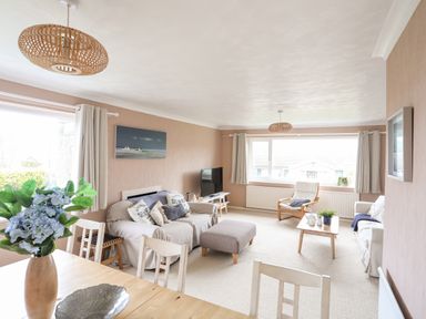 A living room with sofas a coffee table a television and a dining table with flowers at Ty Bedw in Benllech