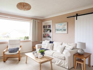 A living room with a white sofa, wooden coffee table, armchair, bookshelf, and side table with a lamp at Ty Bedw in Benllech