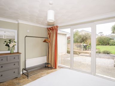 A bedroom with sliding glass doors leading to a garden a dresser with flowers and a clothing rack at Ty Bedw in Benllech