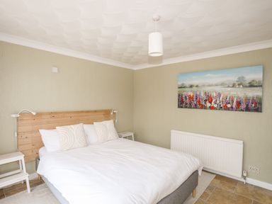 A bedroom with a double bed a wooden headboard and a floral painting on the wall at Ty Bedw in Benllech