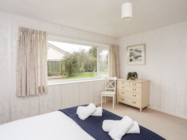 A bedroom with a bed towels dresser chair window and curtains at Ty Bedw in Benllech