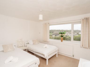 A bedroom with two single beds a chair and a window with curtains and a vase of flowers at Ty Bedw in Benllech