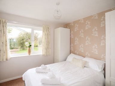 A bedroom with a double bed white wardrobes and a window with curtains at Ty Bedw in Benllech