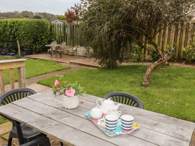 A garden with a wooden table and chairs with a tea set and flowers on the table at Ty Bedw Benllech
