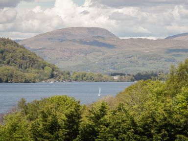 A lake with a sailboat surrounded by trees and hills at Cherry Tree Lodge Calgarth 37 White Cross Bay near Windermere