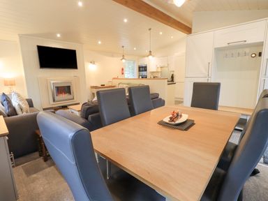 A dining table with chairs next to a living room with sofas and a wall-mounted television at Cherry Tree Lodge Calgarth 37 White Cross Bay near Windermere