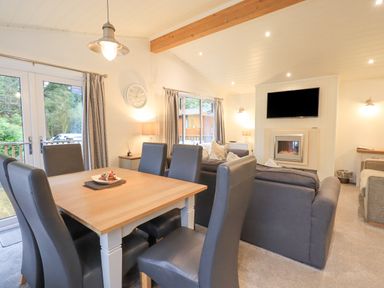 A living room with dining table and chairs a wall-mounted TV and a fireplace at Cherry Tree Lodge Calgarth 37 White Cross Bay near Windermere