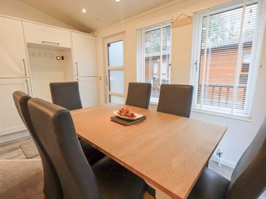 A dining area with a wooden table and six black chairs near windows with blinds at Cherry Tree Lodge Calgarth 37 White Cross Bay near Windermere