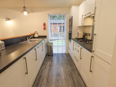 A kitchen with white cabinets a sink stovetop an oven and a window with blinds at Cherry Tree Lodge Calgarth 37 White Cross Bay near Windermere
