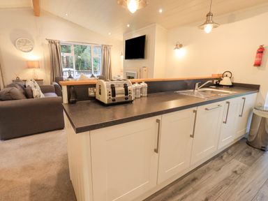 A kitchen area with a sink toaster and kettle and a living room with sofas and a television at Cherry Tree Lodge Calgarth 37 White Cross Bay near Windermere
