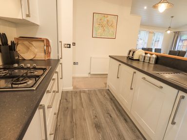 A kitchen with white cabinets a gas stove knives cutting boards a toaster and metal canisters at Cherry Tree Lodge Calgarth 37 White Cross Bay near Windermere