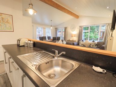 A kitchen sink with countertop and toaster overlooking a living and dining area with sofa and chairs at Cherry Tree Lodge Calgarth 37 White Cross Bay near Windermere