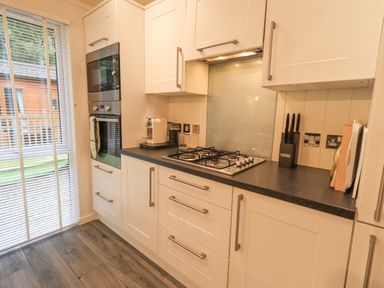 A kitchen with white cabinets a gas stove a built-in oven coffee machines and knives on the counter at Cherry Tree Lodge Calgarth 37 White Cross Bay near Windermere