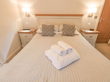 A bedroom with a double bed with striped bedding and patterned cushions two bedside tables with lamps and a wooden door at Cherry Tree Lodge Calgarth 37 White Cross Bay near Windermere