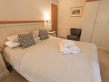 A bedroom with a bed striped bedding folded towels on bed bedside tables armchair and wardrobe at Cherry Tree Lodge Calgarth 37 White Cross Bay near Windermere