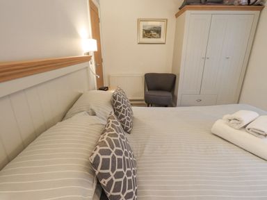 A bedroom with a bed with striped bedding and patterned pillows a gray chair a white wardrobe and towels on the bed at Cherry Tree Lodge Calgarth 37 White Cross Bay near Windermere