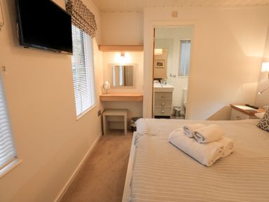 A bedroom with a bed and folded towels a wall-mounted television and a vanity desk with a mirror at Cherry Tree Lodge Calgarth 37 White Cross Bay near Windermere