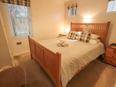 A bedroom with a wooden bed, bedside tables, striped bedding, rolled towels, and windows with blinds at Cherry Tree Lodge Calgarth 37, White Cross Bay near Windermere