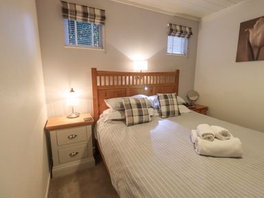 A bedroom with a wooden bed and striped bedding with pillows and towels on the bed at Cherry Tree Lodge Calgarth 37 White Cross Bay near Windermere