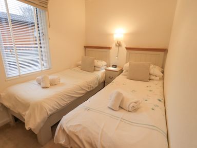 A small bedroom with two single beds a nightstand and a window at Cherry Tree Lodge Calgarth 37 White Cross Bay near Windermere