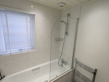 A bathroom with a bathtub shower combination a window with blinds and a chrome towel radiator at Cherry Tree Lodge in Calgarth 37 White Cross Bay near Windermere