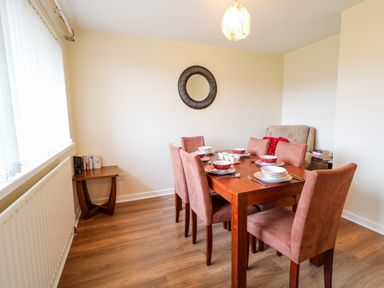 A dining room with a wooden table set for six and pink chairs at 27 Pinewood Hill in Warrenpoint Northern Ireland