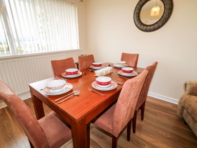 A dining room with a wooden table set for six and six pink chairs at 27 Pinewood Hill in Warrenpoint Northern Ireland