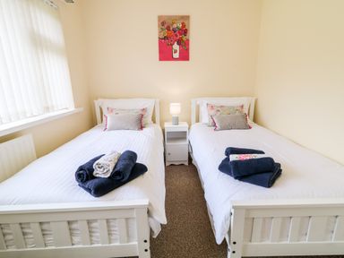 A bedroom with two single beds side by side with white bedding a nightstand with a lamp between them and a painting of flowers on the wall at 27 Pinewood Hill in Warrenpoint Northern Ireland