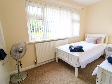 A bedroom with two single beds a standing fan and a window with vertical blinds at 27 Pinewood Hill in Warrenpoint Northern Ireland