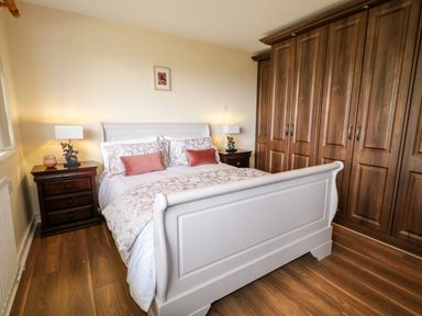 A bedroom with a white bed frame wooden floor bedside tables with lamps and a large wooden wardrobe at 27 Pinewood Hill in Warrenpoint Northern Ireland