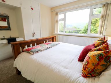 A bedroom with a wooden bed frame a white bedspread colorful pillows a window with a view and built in wardrobe at 27 Pinewood Hill in Warrenpoint Northern Ireland