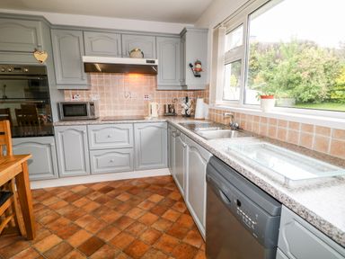 A kitchen with gray cabinets a dishwasher a sink microwave and window with a view of a garden at 27 Pinewood Hill in Warrenpoint Northern Ireland