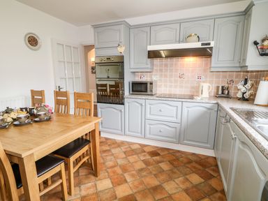 A kitchen with light gray cabinets a wooden dining table with chairs and a tiled floor at 27 Pinewood Hill in Warrenpoint Northern Ireland