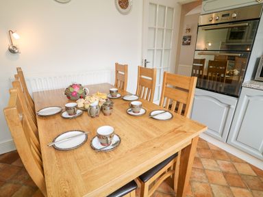 A dining area with a wooden table set with cups plates and cutlery next to a kitchen with an oven at 27 Pinewood Hill in Warrenpoint Northern Ireland