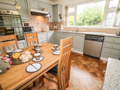 A kitchen with wooden dining table set with cups and plates next to cabinets and appliances at 27 Pinewood Hill in Warrenpoint Northern Ireland