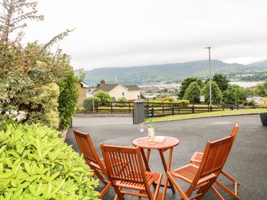 A small outdoor seating area with wooden chairs and a table with a bottle and glasses overlooking a residential neighborhood and hills at 27 Pinewood Hill in Warrenpoint Northern Ireland