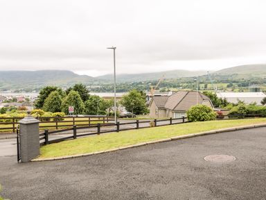 A paved driveway with grass on the side and a fenced road with houses trees and hills in the background at 27 Pinewood Hill Warrenpoint Northern Ireland