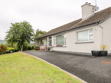 A single-story house with a driveway a lawn trees and flower pots at 27 Pinewood Hill in Warrenpoint Northern Ireland