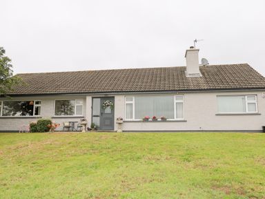 A exterior view of a single story house with a tiled roof and a lawn at 27 Pinewood Hill in Warrenpoint Northern Ireland