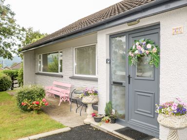 A house entrance with a gray door decorated with a floral wreath pink bench small table with two chairs and flower pots at 27 Pinewood Hill in Warrenpoint Northern Ireland