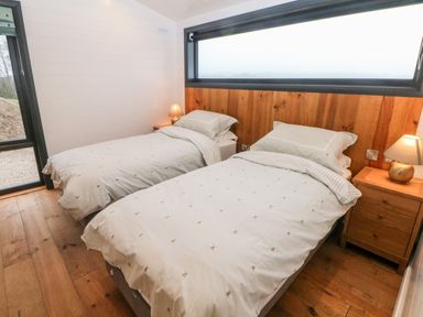 A bedroom with two single beds with white bedding and a wooden headboard next to a nightstand with a lamp at Stables Lodge in Wingerworth