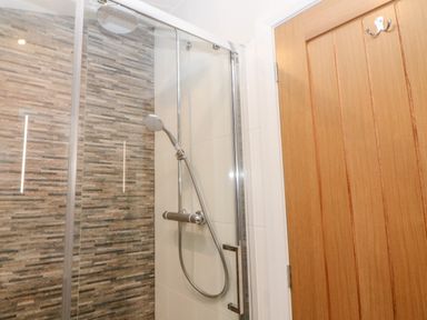 A shower area with a glass door and tiled walls next to a wooden door at Stables Lodge in Wingerworth