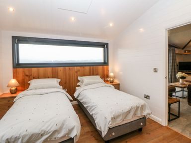 A bedroom with two single beds bedside tables and lamps and a large horizontal window at Stables Lodge in Wingerworth