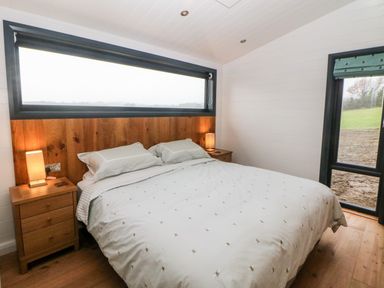 A bedroom with a bed between two bedside tables with lamps and windows showing an outdoor view at Stables Lodge in Wingerworth