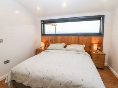 A bedroom with a large bed between two wooden nightstands with lamps and a horizontal window above the wooden headboard at Stables Lodge in Wingerworth