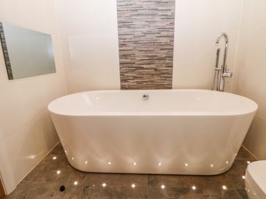 A freestanding bathtub with a floor-mounted faucet and a rectangular mirror on the wall in a bathroom at Stables Lodge in Wingerworth