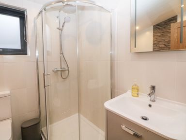 A bathroom with a glass shower enclosure a sink with a mirror and a window at Stables Lodge in Wingerworth